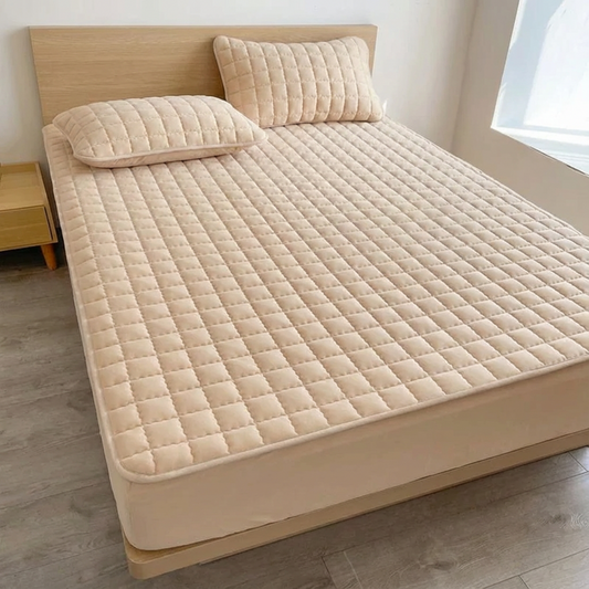 Beige quilted mattress cover on a bed with pillows in a room.