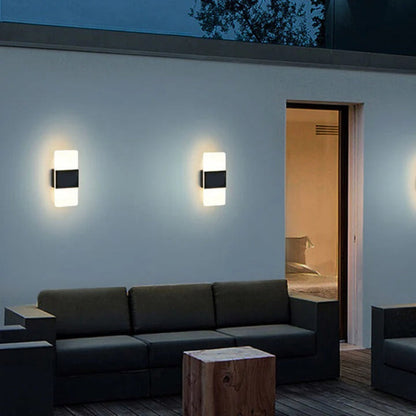 Modern outdoor setting with a dark gray sofa, wooden table, and wall lights on a light blue wall.
