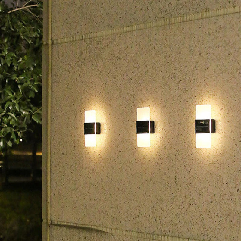 Three wall-mounted outdoor lights on a textured wall with greenery in the background