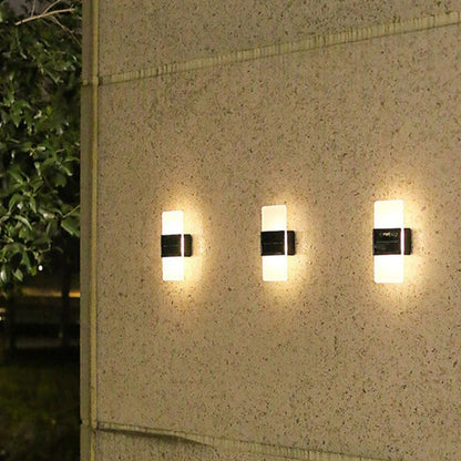 Three wall-mounted outdoor lights on a textured wall with greenery in the background